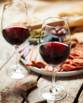 Zwei Weingläser mit Rotwein gefüllt. Im Hintergrund Buschenschankjause